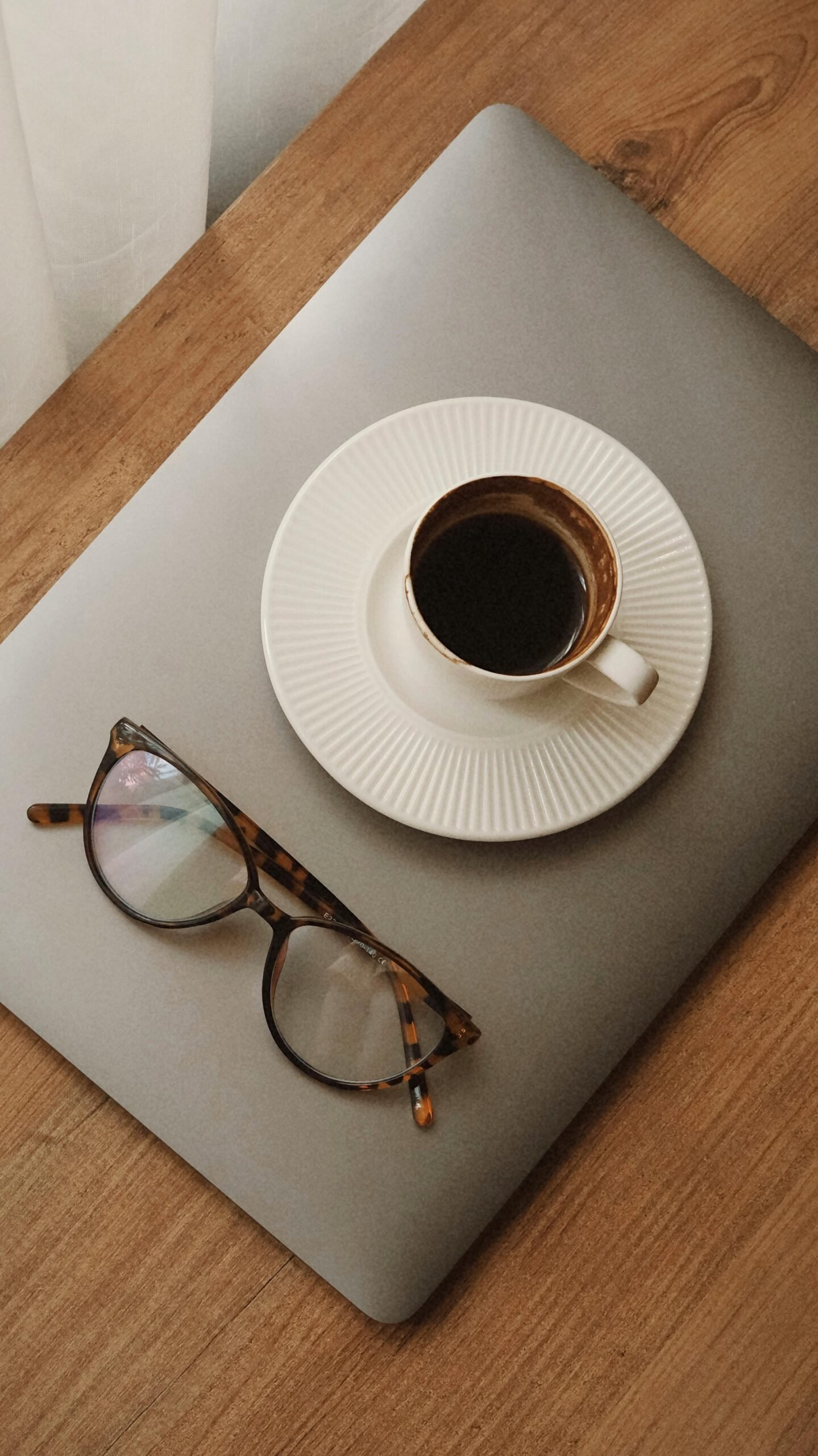 A cup of coffee on a laptop with reading glasses, creating a cozy, productive workspace vibe.