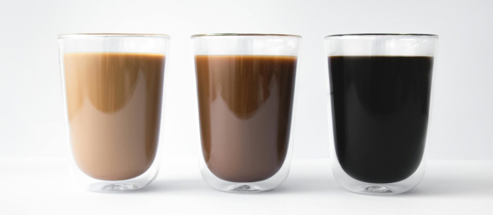 Three glass cups with varying coffee shades in a minimalist setting.